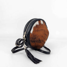 Cargar imagen en el visor de la galería, Bolso bandolera de forma redonda. Delantera de pelo, trasera de piel negra, con bolsillo cerrado con cremallera. Cierra con cremallera. Correa ajustable (no desmontable) de 120cm. Fornituras plateadas. Pompón de adorno con flecos de piel. Forrado interior en tela, con un bolsillo cerrado con cremallera, de LaNievina. Color potro. vista ladeada