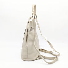 Cargar imagen en el visor de la galería, Mochila de piel lisa. Asa corta para llevar en la mano o brazo, y tirantes ajustables para llevar como mochila. Dos bolsillos delanteros cerrados con cremallera, para llevar a mano las cosas más imprescindibles. Gran capacidad. Muy segura, pues cierra con cremallera por la parte trasera. Interior forrado textil, con bolsillo cerrado con cremallera.La Nievina. Color hueso. Vista lateral