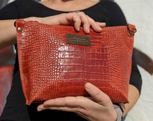 Cargar imagen en el visor de la galería, Bolso bandolera de mujer, piel vacuno, efecto escamas, de tamaño mediano, cierra con cremallera, de LaNievina. Color rojo brillo, detalle en manoBolso bandolera en piel vacuno, efecto escamas Cuadro pequeño de piel negra cosido como adorno en un de los frontales. Correa de 110 cm. ajustable, en piel del mismo color, con anillas y ganchos en latón envejecido. Interior forrado en tela color negro, con bolsillo cerrado con cremallera. De LaNievina. Color rojo brillo, en la mano