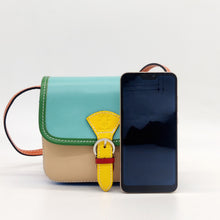 Cargar imagen en el visor de la galería, Bolso bandolera de piel de varios colores. Doble compartimento interior, más bolsillo con cremallera. Cierra con clip imantado. Asa de piel ajustable. Colores juveniles, muy alegre, de LaNievina.Vista con movil para referencia de tamaño