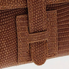 Cargar imagen en el visor de la galería, Cartera clutch en piel rígida. Cierra con solapa y cinta de piel. Dos correas adicionales: una corta para llevarla en la muñeca y otra larga ajustable (aprox. 110 cm.) para poder llevarla también como bandolera si se necesitan las manos libres. Interior en piel, no forrado, con pequeño compartimento plano sin cierre. De LaNievina, detalle del cierre.