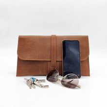 Cargar imagen en el visor de la galería, Cartera clutch en piel rígida. Cierra con solapa y cinta de piel. Dos correas adicionales: una corta para llevarla en la muñeca y otra larga ajustable (aprox. 110 cm.) para poder llevarla también como bandolera si se necesitan las manos libres. Interior en piel, no forrado, con pequeño compartimento plano sin cierre. De LaNievina, con contenido para referencia de tamaño.