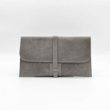 Cargar imagen en el visor de la galería, Cartera clutch en piel rígida. Cierra con solapa y cinta de piel. Dos correas adicionales: una corta para llevarla en la muñeca y otra larga ajustable (aprox. 110 cm.) para poder llevarla también como bandolera si se necesitan las manos libres. Interior en piel, no forrado, con pequeño compartimento plano sin cierre. De LaNievina, color gris.