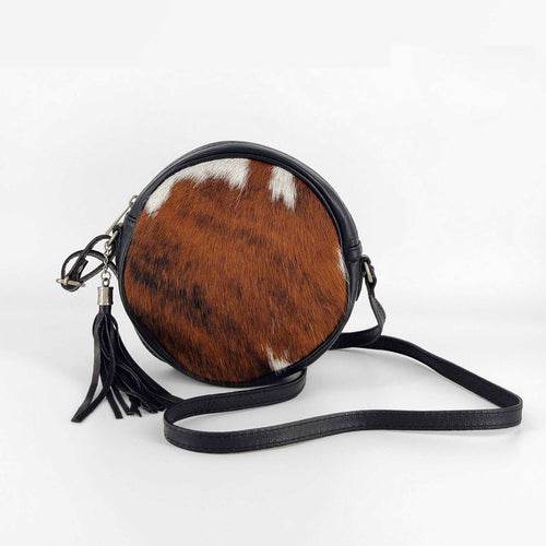 Bolso bandolera de forma redonda. Delantera de pelo, trasera de piel negra, con bolsillo cerrado con cremallera. Cierra con cremallera. Correa ajustable (no desmontable) de 120cm. Fornituras plateadas. Pompón de adorno con flecos de piel. Forrado interior en tela, con un bolsillo cerrado con cremallera, de LaNievina. Color potro