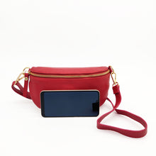 Cargar imagen en el visor de la galería, Bolso tipo riñonera de piel lisa. Cierra con cremallera. Asa larga de piel ajustable. Interior forrado textil, con bolsillo cerrado con cremallera. Tamaño mediano. La Nievina.  Vista frontal con movil para referencia de tamaño
