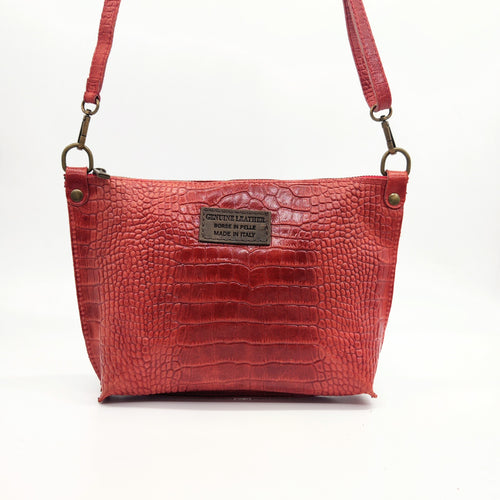 Bolso bandolera en piel vacuno, efecto escamas Cuadro pequeño de piel negra cosido como adorno en un de los frontales. Correa de 110 cm. ajustable, en piel del mismo color, con anillas y ganchos en latón envejecido. Interior forrado en tela color negro, con bolsillo cerrado con cremallera. De LaNievina. Color rojo brillo, vista frontal colgado
