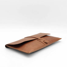 Cargar imagen en el visor de la galería, Cartera clutch en piel rígida. Cierra con solapa y cinta de piel. Dos correas adicionales: una corta para llevarla en la muñeca y otra larga ajustable (aprox. 110 cm.) para poder llevarla también como bandolera si se necesitan las manos libres. Interior en piel, no forrado, con pequeño compartimento plano sin cierre. De LaNievina, vista tumbado
